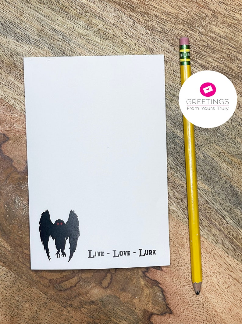 Peut inclure: Une carte blanche avec une silhouette noire d'une cr&eacute;ature aux grandes ailes et aux yeux rouges. Le texte "Live - Love - Lurk" est imprim&eacute; sous la cr&eacute;ature.