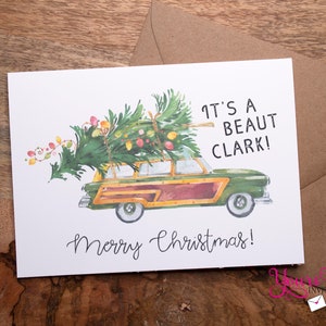 May include: A Christmas card featuring a watercolor illustration of a vintage station wagon with a Christmas tree strapped to the roof. The text on the card reads "It's a beaut Clark! Merry Christmas!"