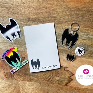 Peut inclure: Un ensemble de produits d&eacute;riv&eacute;s sur le th&egrave;me de Mothman comprenant un autocollant avec une finition holographique arc-en-ciel, un porte-cl&eacute;s, un petit autocollant, une carte de v&oelig;ux et un autocollant rond. La carte de v&oelig;ux porte l'inscription "Live - Love - Lurk". Les autocollants et le porte-cl&eacute;s pr&eacute;sentent une silhouette noire de Mothman avec des yeux rouges.