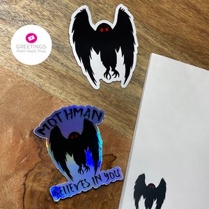 Peut inclure: Trois autocollants repr&eacute;sentant une silhouette noire du Mothman, une cr&eacute;ature cryptide aux grands yeux et aux ailes. Un autocollant est iridescent et dit "Mothman Believes in You". Un autre autocollant est noir et blanc et dit "Live - Love - Lure".