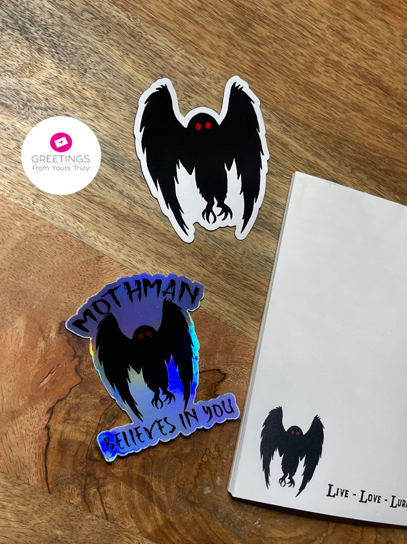 Peut inclure: Trois autocollants repr&eacute;sentant une silhouette noire du Mothman, une cr&eacute;ature cryptide aux grands yeux et aux ailes. Un autocollant est iridescent et dit "Mothman Believes in You". Un autre autocollant est noir et blanc et dit "Live - Love - Lure".
