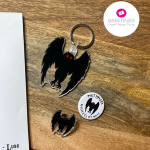 Peut inclure: Un porte-cl&eacute;s Mothman noir et blanc avec des yeux rouges et le texte "Mothman Believes in You". Le porte-cl&eacute;s est attach&eacute; &agrave; un anneau de cl&eacute; argent&eacute;. Il y a aussi une petite &eacute;pingle Mothman noir et blanc avec des yeux rouges.