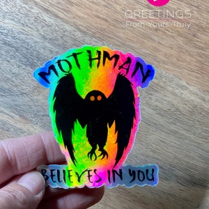 Peut inclure: Un autocollant holographique avec une silhouette noire de Mothman, une cr&eacute;ature cryptide aux grandes ailes et aux yeux rouges brillants. L'autocollant a des couleurs arc-en-ciel iris&eacute;es et le texte "Mothman Believes in You".