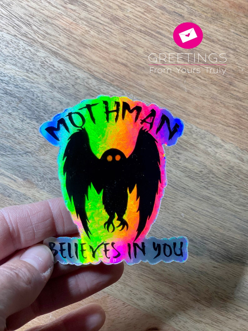 Peut inclure: Un autocollant holographique avec une silhouette noire de Mothman, une cr&eacute;ature cryptide aux grandes ailes et aux yeux rouges brillants. L'autocollant a des couleurs arc-en-ciel iris&eacute;es et le texte "Mothman Believes in You".
