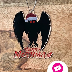 May include: A black and red Christmas ornament featuring a silhouette of the Mothman wearing a Santa hat with the text "Merry Mothmas".