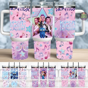 Può includere: Bicchieri isolati con manici e coperchi bianchi. I bicchieri presentano un design rosa con note musicali, stelle e il testo "HUNTRIX" e "K-POP DEMON HUNTERS". Un bicchiere ha una grafica di tre donne e un gatto blu.