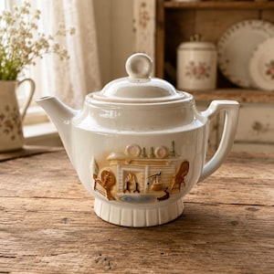 May include: A cream-colored ceramic teapot with a lid and a handle. The body features a raised, three-dimensional relief design depicting a fireplace scene with a spinning wheel, a chair, and various hearth tools in shades of brown and tan.