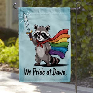 May include: A rectangular garden flag featuring a cartoon raccoon wearing a rainbow-colored cape and a red neckerchief. The raccoon holds a silver sword aloft against a light blue background. The text "We Pride at Dawn," is printed in black.