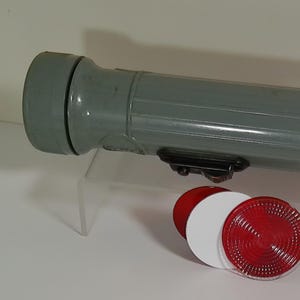 May include: A grey flashlight with a black handle and a red lens. The flashlight is cylindrical and has a textured surface. There are also two additional lenses, one red and one white.