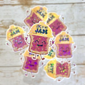 May include: A collection of glittery stickers featuring a smiling cartoon piece of toast with jam. The toast has arms and legs and the text "LDC IS MY JAM" is on the top of the toast.