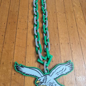 May include: A green and gray plastic chain with a green and white eagle pendant. The eagle is holding a football.