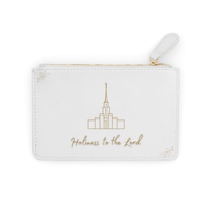 Puede incluir: Bolsa blanca con cremallera con un dibujo lineal dorado de un edificio y las palabras "Holiness to the Lord" en escritura dorada. La bolsa tiene un tirador de cremallera blanco y una cremallera dorada.