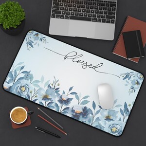 May include: A rectangular mousepad with a floral design in shades of blue and green. The word "Blessed" is written in cursive across the top. A white mouse, laptop, and other office supplies are on the dark surface.