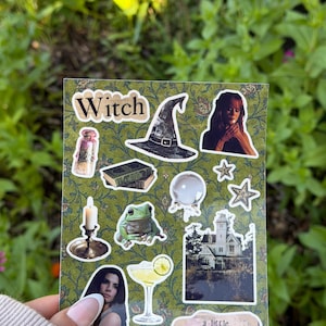 May include: A rectangular sticker sheet with a green floral background featuring various die-cut stickers including a witch hat, a crystal ball, a frog, a candle, a cocktail, a house, two stars, two books, a potion bottle, and two portraits with the text Witch and a little Practical Magic.