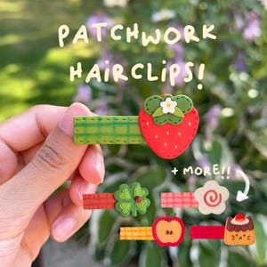 Pode incluir: Várias presilhas de cabelo patchwork coloridas são apresentadas. Apresentam vários desenhos: morango vermelho, trevo de quatro folhas, flor, maçã e bolo. O texto "PATCHWORK HAIRCLIPS! + MORE!!" é visível.
