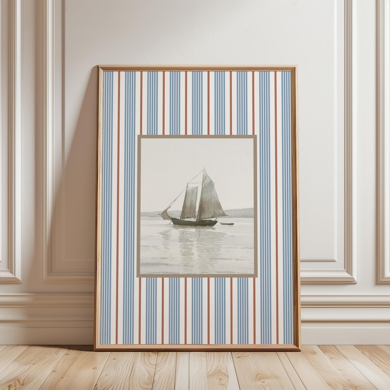 May include: Framed nautical art print featuring a sailboat on the water. The artwork is set within a brown frame and a striped background of blue, red, and white vertical lines. The print is displayed against a white wall.
