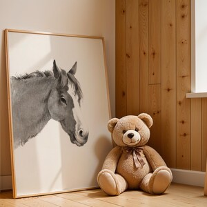 May include: A framed watercolor print of a horse's head in shades of gray and white. A large, plush teddy bear with a brown ribbon sits next to the artwork. The room has wooden paneling and a small wooden ladder.