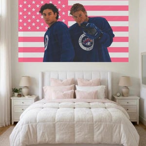 Puede incluir: Un póster de pared rectangular grande que muestra a dos personas con camisetas deportivas de manga larga de color azul oscuro con un logotipo circular que dice Briar U Hawks. El fondo del póster es una bandera estadounidense estilizada con rayas rosas y blancas.