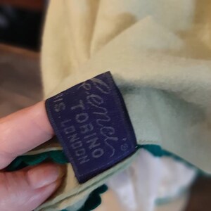 May include: A green and white garment with a blue label that reads "Renzi's Torino, N.S. London".
