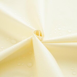 May include: Close-up of a pale yellow fabric with water droplets. The fabric is folded and rolled, creating a spiral shape. The material appears smooth and possibly water-resistant, with visible water beads.