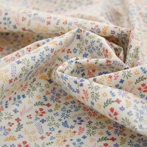 May include: A white fabric with a small floral pattern in shades of blue, red, yellow, and green. The fabric is folded in a way that shows the pattern.