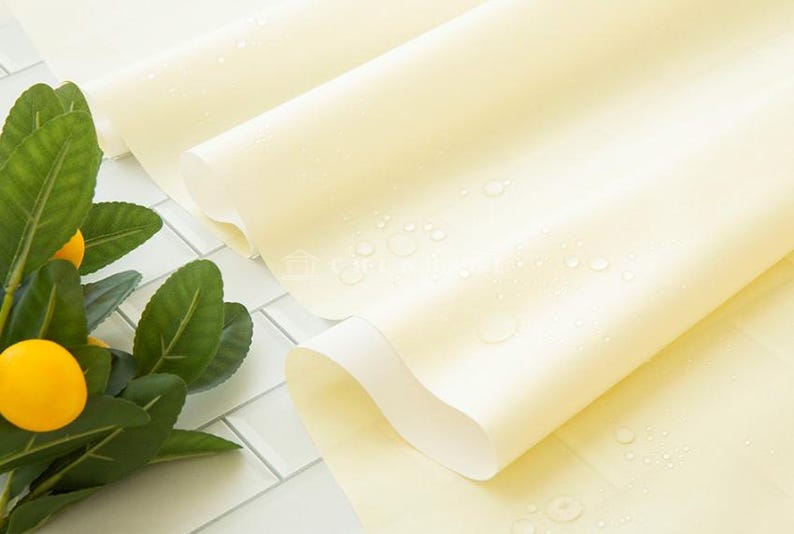 May include: A close-up shot of rolled, pale yellow fabric with water droplets, possibly a tablecloth or similar textile. A sprig of lemons with green leaves is in the corner, suggesting a fresh, natural theme.