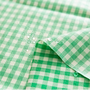 May include: Close-up of a green and white checkered fabric with water droplets on the surface. The fabric is folded, revealing the pattern and texture. The gingham pattern is a classic design.