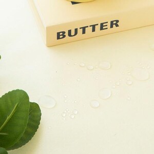 May include: A close-up shot of a light yellow surface with water droplets and green leaves. The word "BUTTER" is printed in black on a light yellow rectangular object.