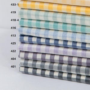 May include: A stack of fabric samples in various colors, each with a classic gingham check pattern. Colors include yellow, green, teal, blue, purple, and gray. The fabric is neatly folded, showcasing the different color options available.