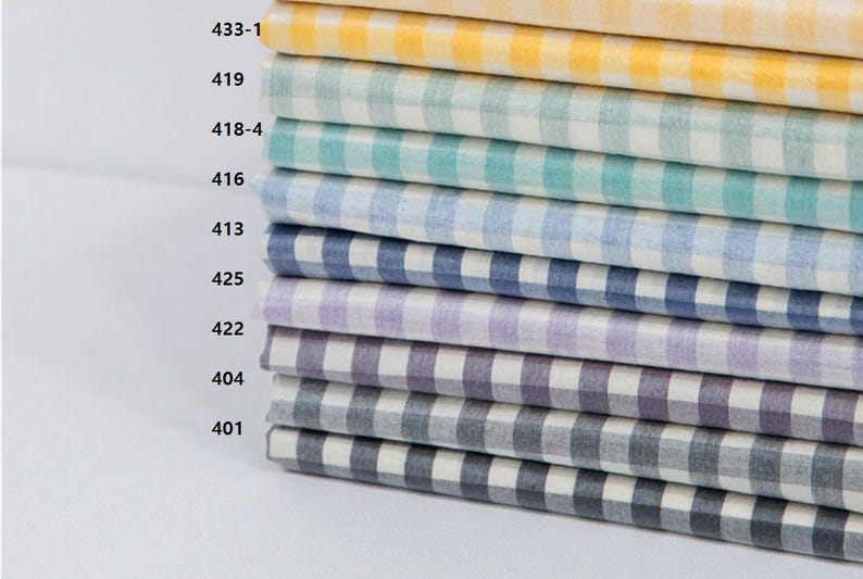 May include: A stack of fabric samples in various colors, each with a classic gingham check pattern. Colors include yellow, green, teal, blue, purple, and gray. The fabric is neatly folded, showcasing the different color options available.