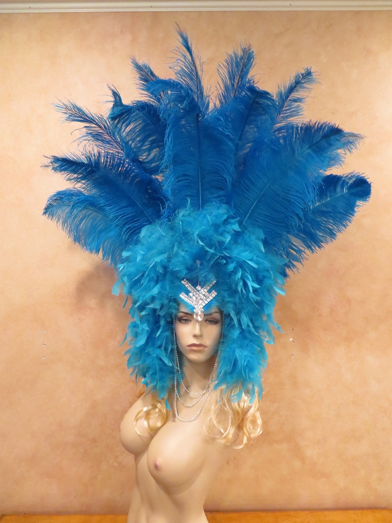 K&ouml;nnte beinhalten: Ein blauer Federkopfschmuck mit einem gro&szlig;en, funkelnden Strass-Stirnband. Der Kopfschmuck besteht aus blauen Federn und hat ein flauschiges, mehrschichtiges Design.