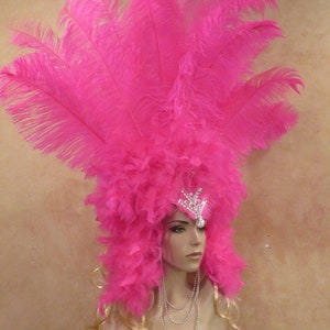 K&ouml;nnte beinhalten: Ein rosa Federkopfschmuck mit einer Juwelenkrone und einer Perlenkette. Der Kopfschmuck besteht aus gro&szlig;en, flauschigen Federn und ist perfekt f&uuml;r ein Kost&uuml;m oder eine Party.