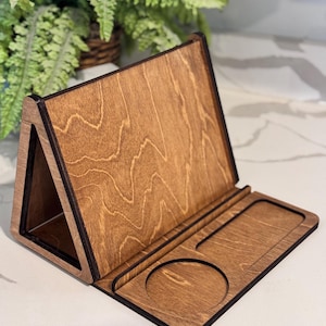 May include: A brown wooden desk organizer featuring a triangular upright stand for a tablet or phone and a flat base with a circular cutout and a rectangular recessed tray for holding small items, showcasing a natural wood grain finish.