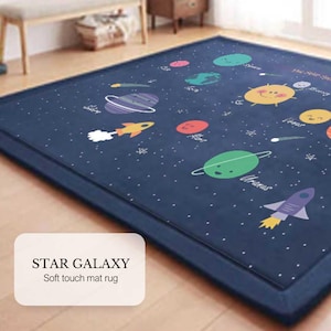 May include: A blue and white soft touch mat rug with a space theme. The rug features a cartoon sun, planets, stars, and rockets. The text "STAR GALAXY" and "Soft touch mat rug" is printed on the rug.