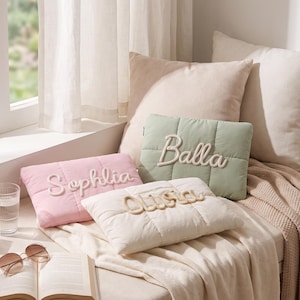 Peut inclure: Trois pochettes rectangulaires matelassées en rose pastel, vert sauge et crème. Chaque pochette présente un nom brodé en lettres de cordon blanc ou crème en relief : Sophlia sur le rose, Balla sur le vert et Olisa sur la pochette crème.