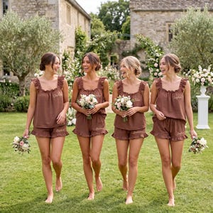 May include: Four matching sets of brown sleeveless tops and ruffled shorts, each featuring embroidered names on the chest and leg. The tops have wide straps and a square neckline, while the shorts have a relaxed fit with a ruffled hemline.