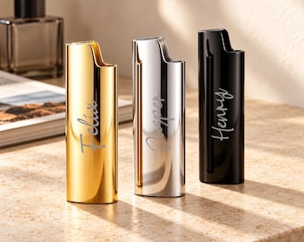 Puede incluir: Tres encendedores de metal con un acabado liso y reflectante en oro, plata y negro. Cada encendedor presenta un nombre grabado personalizado en letra cursiva: Felix en el dorado, Jasper en el plateado y Henry en el encendedor negro.