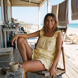 May include: A pale yellow two-piece pajama set featuring a sleeveless top with ruffled straps and matching shorts with ruffled hems. The top is embroidered with the name Amelia, and the shorts are embroidered with the word Bride in script.