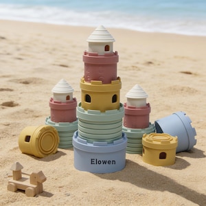 Puede incluir: Un conjunto de castillos de juguete apilables y coloridos en tonos rosa, amarillo, azul y verde, con tejados cónicos blancos. La palabra "Elowen" está impresa en una de las bases azules. También hay un pequeño tren de juguete de madera.