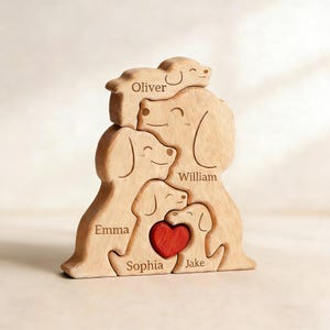 Puede incluir: Un rompecabezas de madera de una familia de perros con cinco perros apilados. Los perros de color marrón claro tienen los nombres grabados: Oliver, William, Emma, Sophia y Jake. Un corazón rojo está en el centro.