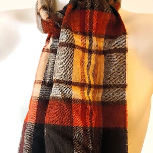 May include: A plaid scarf in shades of red, orange, black, and gray, displayed on a mannequin. The scarf has a fringed edge and a classic, warm design, suitable for fall and winter wear.