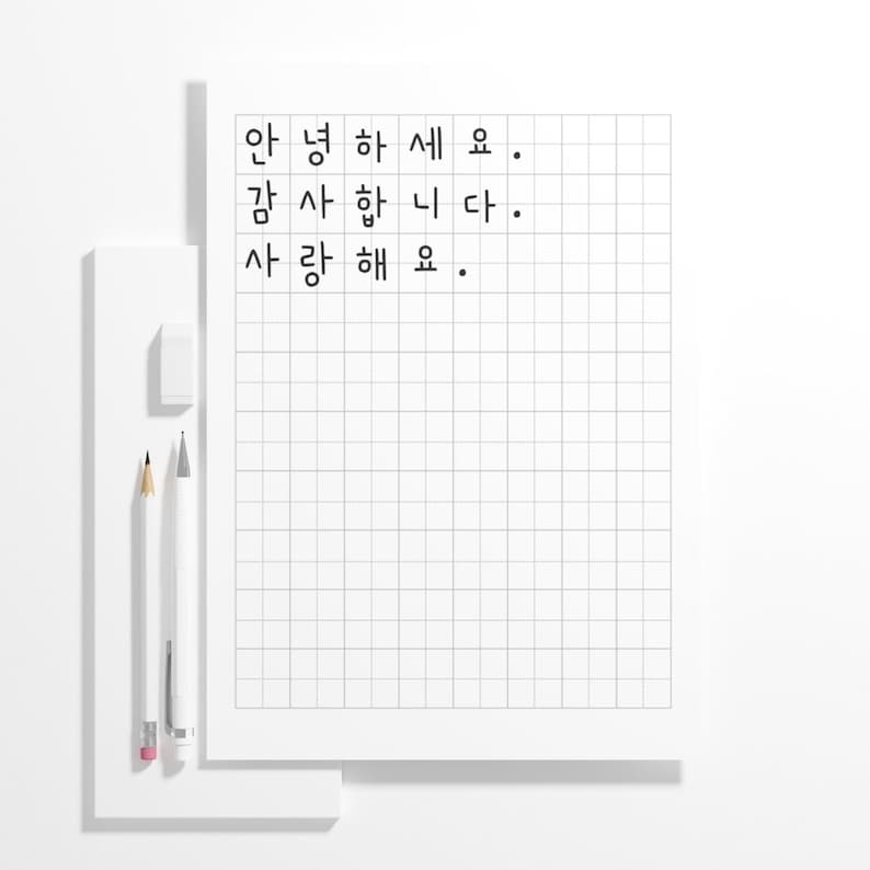 May include: A white notepad with a grid pattern and Korean text. The words "안녕하세요, 감사합니다, 사랑해요" are written in black. A white eraser, a yellow pencil, and a white pencil are on the left.