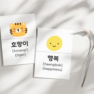 May include: Two white cards with Korean text and illustrations. One card features a cartoon tiger with the Korean word "호랑이" and the English translation "tiger." The other card shows a smiling yellow circle with the Korean word "행복" and the English translation "happiness."