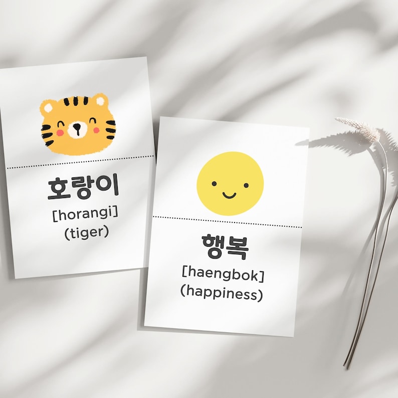 May include: Two white cards with Korean text and illustrations. One card features a cartoon tiger with the Korean word "호랑이" and the English translation "tiger." The other card shows a smiling yellow circle with the Korean word "행복" and the English translation "happiness."
