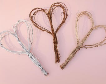 Könnte beinhalten: Drei Zweig-Herzkranz in verschiedenen Farben: Weiß, Braun und Natur. Die Kränze sind aus dünnen Zweigen gefertigt und haben die Form von Herzen. Sie sind perfekt, um Ihrem Zuhause einen rustikalen Touch zu verleihen.