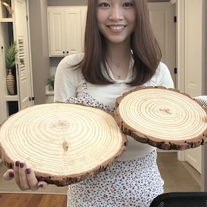 Puede incluir: Dos rodajas de madera redondas con anillos de crecimiento visibles y bordes de corteza natural. La madera clara contrasta con la corteza más oscura, mostrando la veta y la textura naturales. Ideales para proyectos decorativos o artesanales.