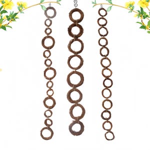 Op de afbeelding: Drie strengen bruine takkransen die aan een plafond hangen. Elke streng bestaat uit 10 kransen, verbonden door een metalen ring.