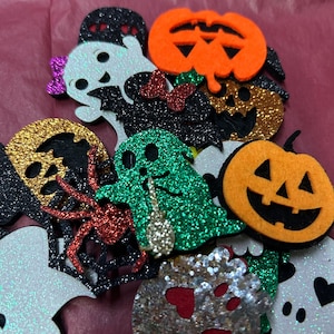 Könnte beinhalten: Eine Sammlung von glitzernden Filz-Halloween-Dekorationen, darunter orangefarbene Kürbisse, weiße und grüne Geister, eine rote Spinne und schwarze Fledermäuse. Die Formen weisen ausgeschnittene Gesichtsdetails und kleine dekorative Schleifen auf.