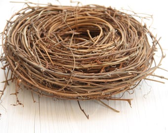 May include: A brown twig wreath, made of natural branches, is a circular nest-like shape. The wreath is on a white surface.