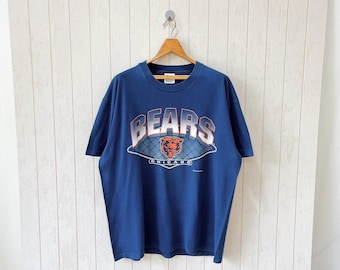 May include: Navy blue t-shirt with the word "BEARS" in a gradient design above a Chicago Bears logo. The shirt is hanging on a wooden hanger against a white background.